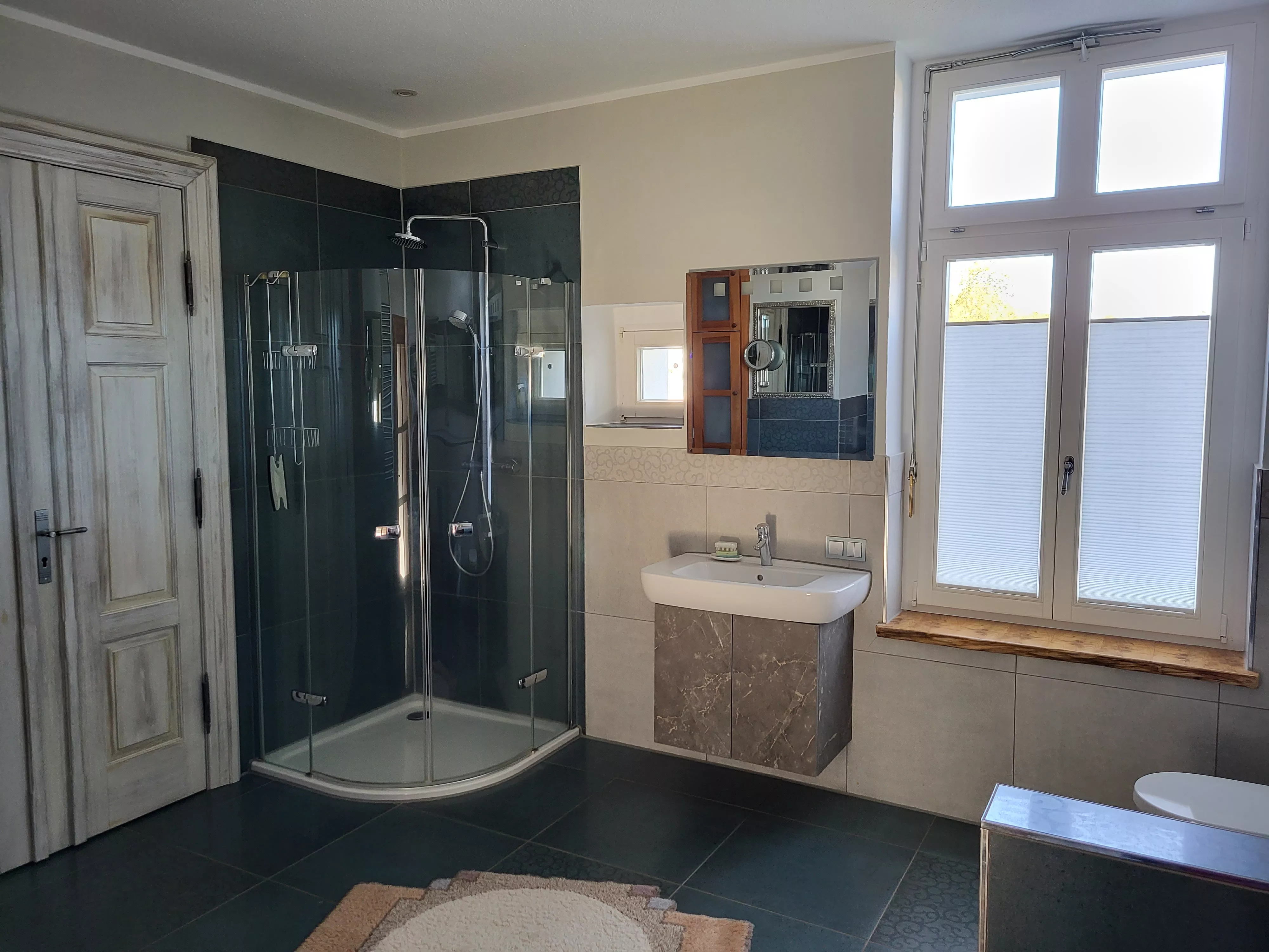 Modernes Badezimmer mit ebenerdiger Rundduschkabine aus Glas, wandhängendem Waschtisch mit Marmorunterschrank und Sprossenfenster